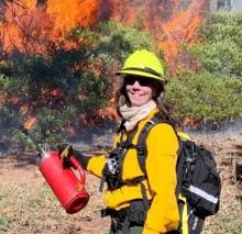 Kristen Wilson holding a drip torch in front of a prescribed fire